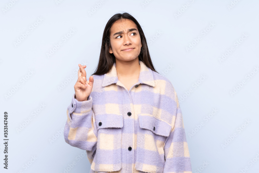 Young Indian woman isolated on blue background with fingers crossing and wishing the best Young Indian woman isolated on blue background with fingers crossing and wishing the best