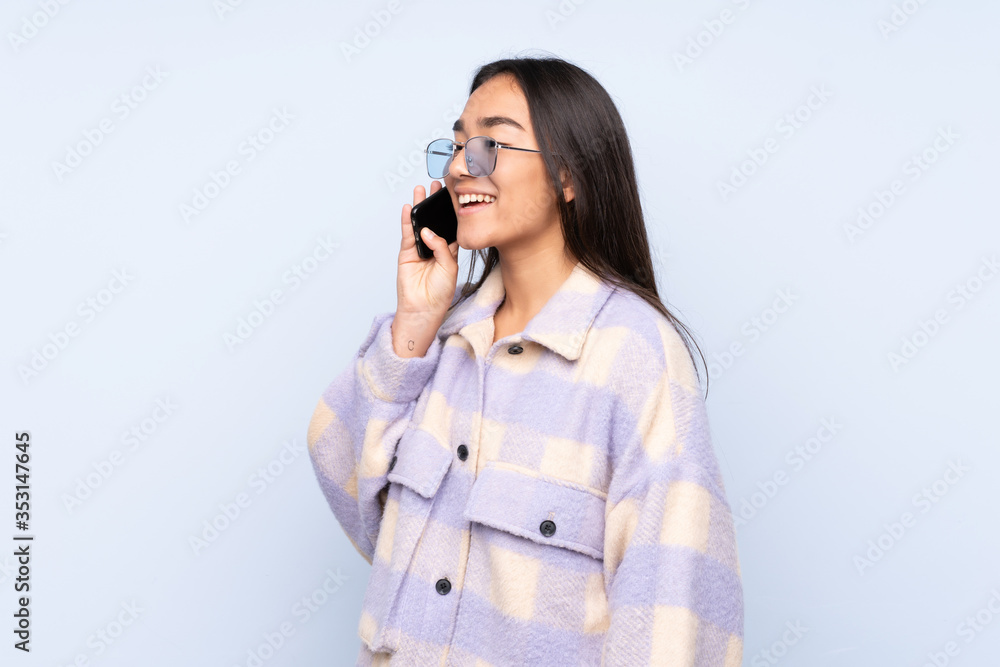 Young Indian woman isolated on blue background keeping a conversation with the mobile phone Young Indian woman isolated on blue background keeping a conversation with the mobile phone