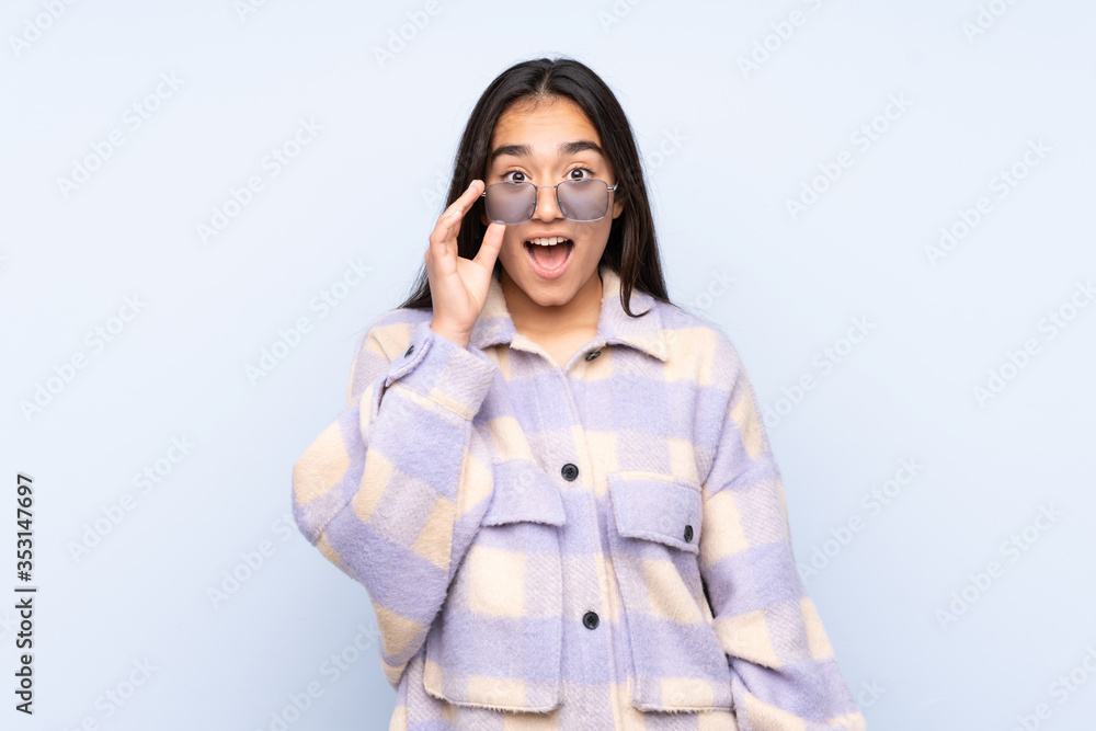 Young Indian woman isolated on blue background with glasses and surprised Young Indian woman isolated on blue background with glasses and surprised