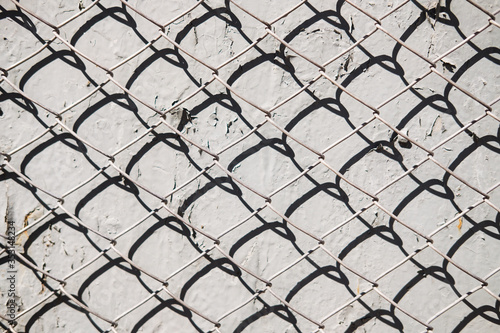 Metal mesh pattern on concrete wall background with shadow. Abstract texture.