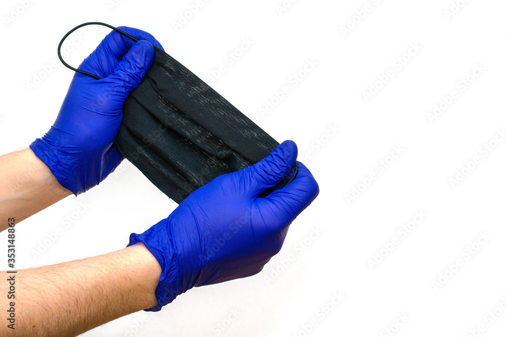 hands in blue medical gloves hold a black hygiene mask on the white background hands in blue medical gloves hold a black hygiene mask on the white background