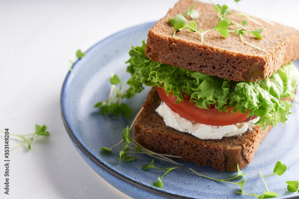 healthy sandwich with gluten-free bread, tomato, lettuce and germinated microgreens served in plate on white table