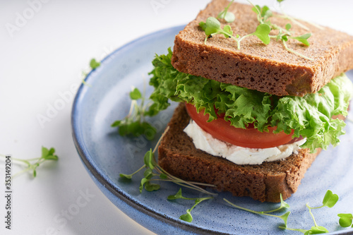 healthy sandwich with gluten-free bread  tomato  lettuce and germinated microgreens served in plate on white table