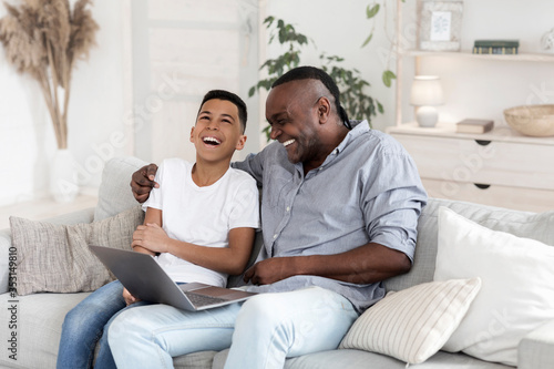 Preteen Black Boy Watching Comedy Movie On Laptop With Grandfather And Laughing