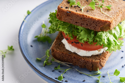 healthy sandwich with gluten-free bread, tomato, lettuce and germinated microgreens, sprinkled with sesame seeds served in plate
