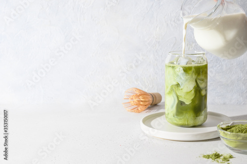 Photographie Iced Green matcha latte tea and pouring milk in glass on white background