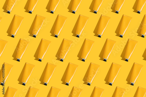 Pattern of yellow tubes of sunscreen on bright yellow background with hard shadow. Sun protection in the summer.
