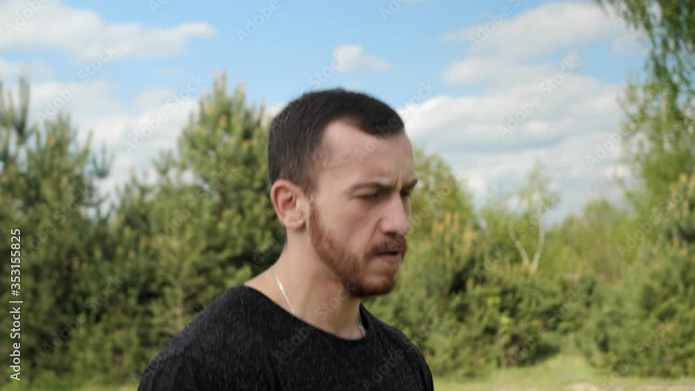 Man with muscular does warm-up runs on the spot and jumps on a background of green trees with a beautiful sky.