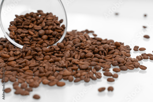 Coffee beans pour out of a glass bowl onto a light surface. coffee background, close-up