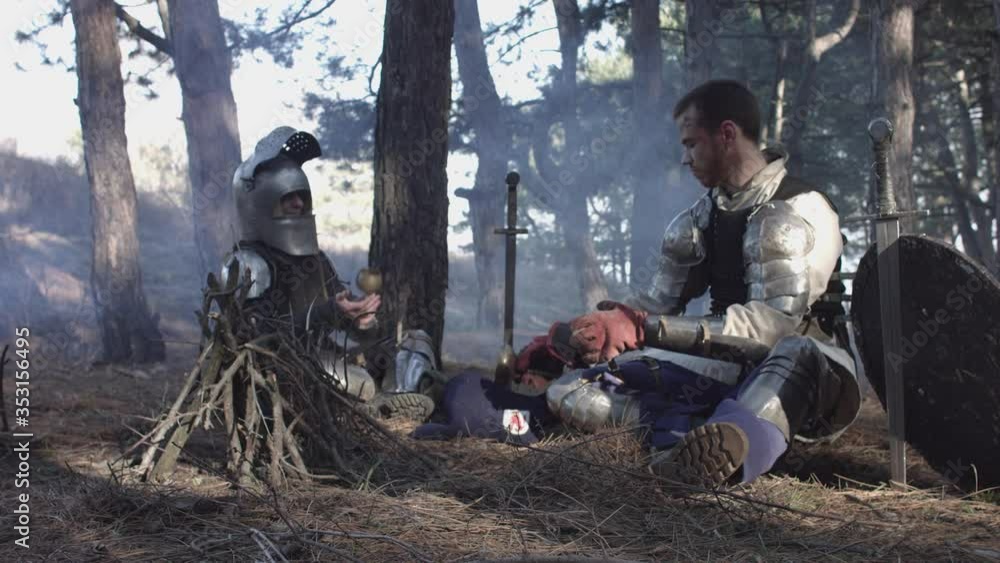 Two medieval knights sitting near bonfire and devide production Two medieval knights sitting near bonfire and devide production