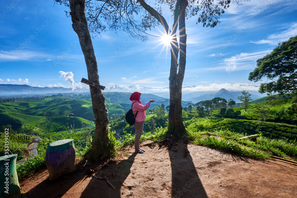 Muslim woman traveler enjoys a sunny morning and scenic view of tea plantation in South Bandung, Indonesia