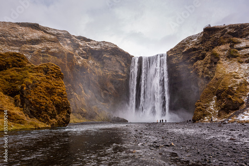 Skogafoss waterfall in South Iceland. Tourists admiring the waterfall. Popular and famous tourist attraction.