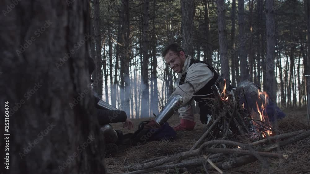 Two medieval knights sitting near bonfire and devide production Two medieval knights sitting near bonfire and devide production