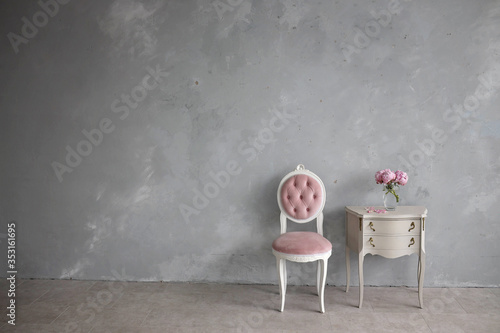Minimalistic interior in the Baroque style. Vintage bedside table,a chair, a medallion with four wheel brace. Grey loft wall.
