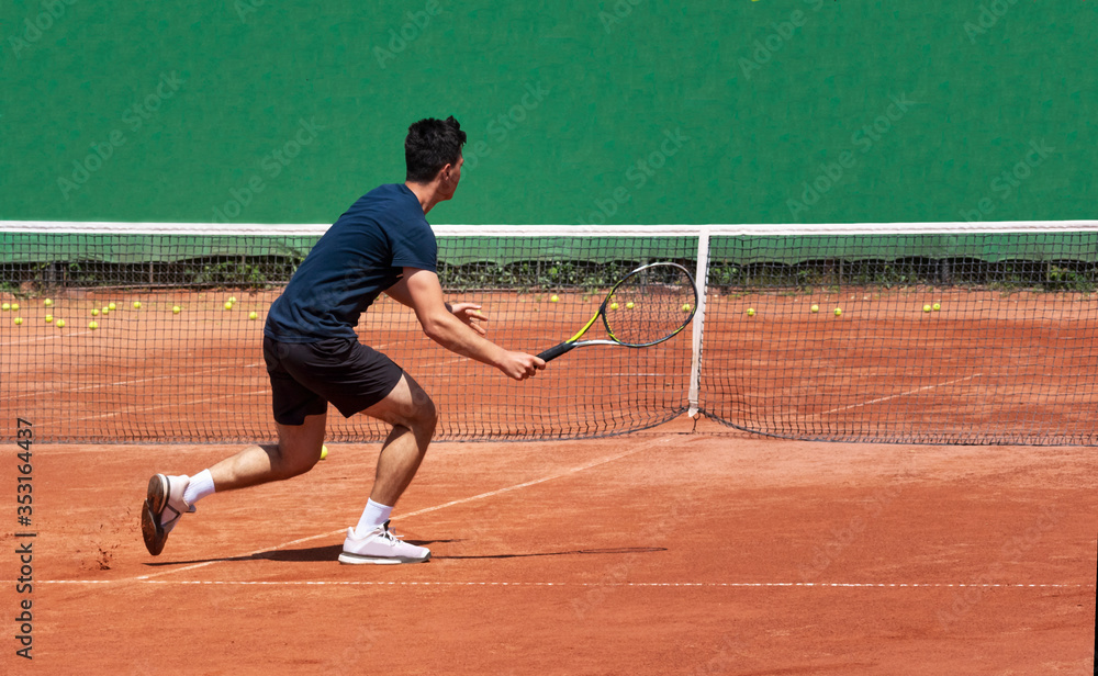 Professional tennis player on the court with a racket plays by the net. A young man plays on a clay tennis court. Teenager tennis player. Back view. Copy space for text.