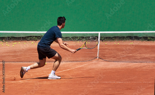 Professional tennis player on the court with a racket plays by the net. A young man plays on a clay tennis court. Teenager tennis player. Back view. Copy space for text. © Elena