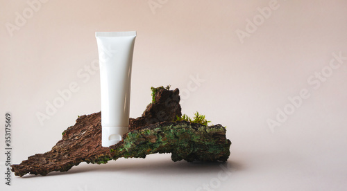 White plastic tube with facial moisturizer cream or facial cleanser on tree bark on beige background with copy space. Concept bio organic beauty products with natural extract and vitamin