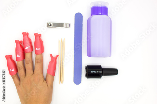 Female hand removing shellac during manicure procedure, flat lay on white background. Woman painting her nails with gel nail polish, tools, manicure set, view from above. Home shellac nail care