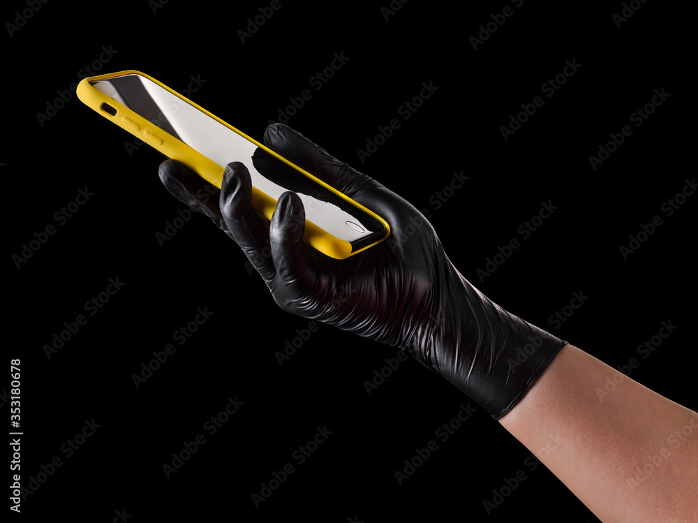 Obraz premium Hand in black glove holding mobile phone with blank screen isolated on black