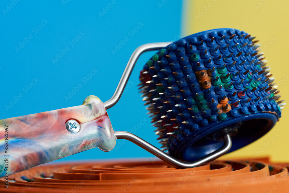 A blue massager with rubber and spikes, metal needles, lie on a green ribbon on a yellow-blue background. Advertising, For relaxation and health A blue massager with rubber and spikes, metal needles, lie on a green ribbon on a yellow-blue background. Advertising, For relaxation and health