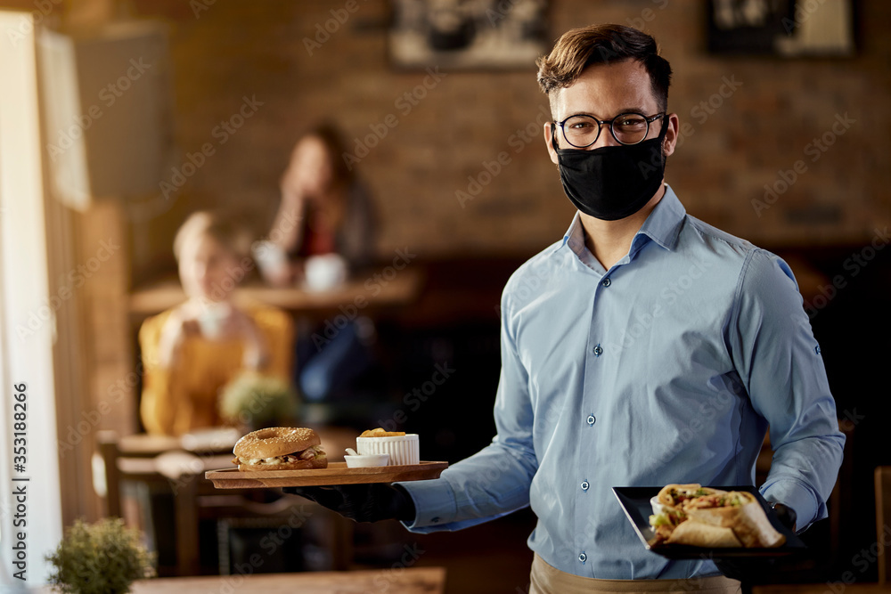 Happy waiter serving food while wearing protective face mask in a pub. - obrazy, fototapety, plakaty 