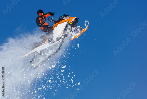 Extreme sport race snowmobiles. Snowmobile in high jump above track. Sportsman on snowmobile. Winter competition  sunny day. Trick against blue sky. Snow motor sports Copy space.