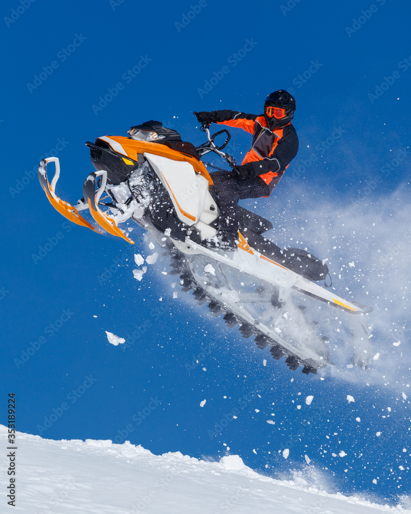 snowmobile rider jumping through snow. RIDER MAN WITH HELMET JUMPING WITH SNOWMOBILE BETWEEN SKY ON WINTER. a bright suit and a snow motorcycle. Extreme winter sport. high resolution and photo quality