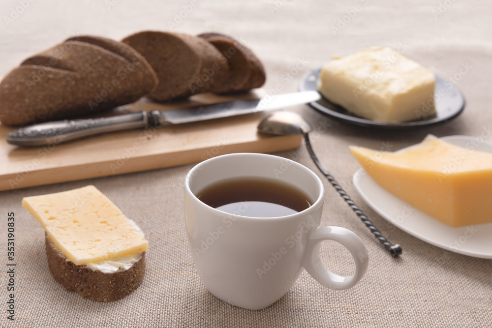 Sliced bread and knife on a cutting board. Butter, cheese, a cup of coffee on a sackcloth. Side view breakfast brunch on table concept Sliced bread and knife on a cutting board. Butter, cheese, a cup of coffee on a sackcloth. Side view breakfast brunch on table concept