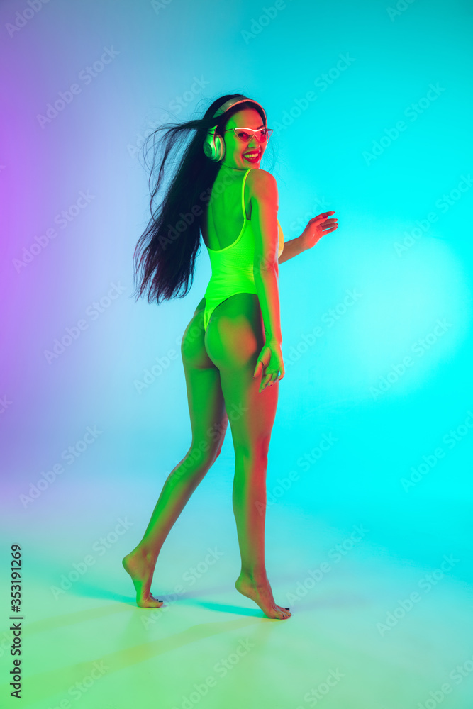Beautiful young girl dancing with wireless headphones on gradient studio background in neon light. Woman in fashionable bodysuit. Facial expression, summer, weekend, beauty, resort concept. Vacations. Beautiful young girl dancing with wireless headphones on gradient studio background in neon light. Woman in fashionable bodysuit. Facial expression, summer, weekend, beauty, resort concept. Vacations.