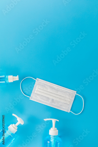 Top view medical face mask and 3 Different bottle alcohol gel on light blue background with copy space. Face mask and hand sanitizer gel in pump head bottle.