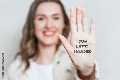 Fotografía Left-handed girl shows her left hand to the camera and smiles isolated over gray