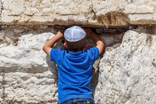 A little Jewish boy prays at the Western wall in Jerusalem. Notes with prayers and wishes in the crack between the stones.