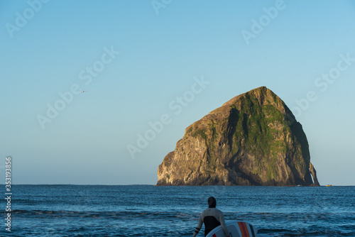 man carrying surfboard at oceans' edge at Cape Kiwanda in Oregon