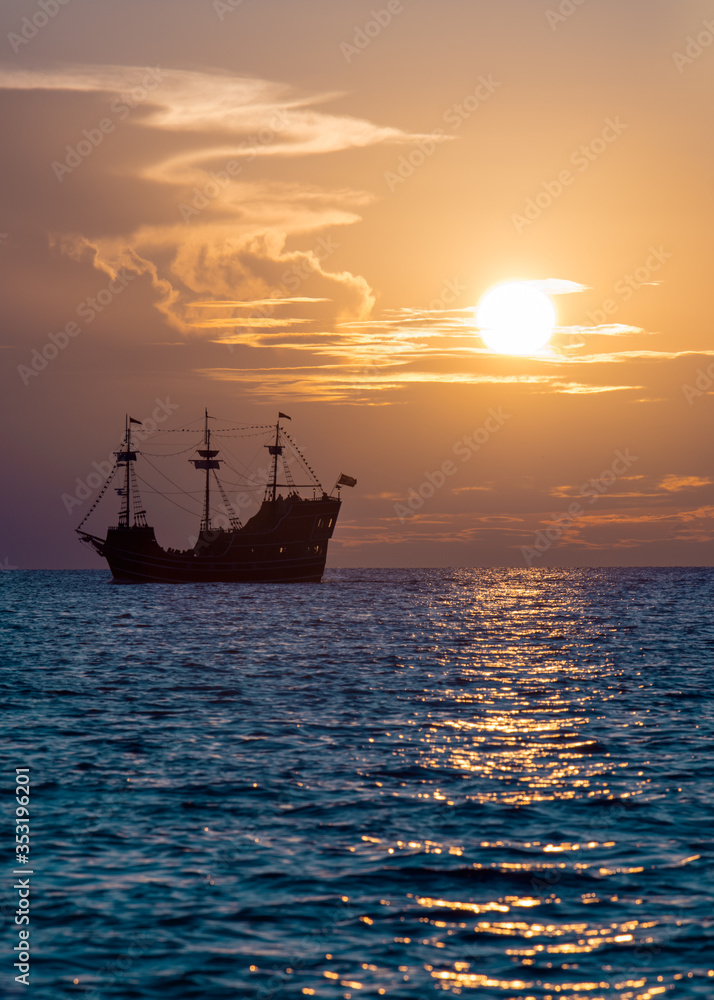 Pirate ship. Retro or antique sailboat. Ocean sunset. Sunny glare on the water.