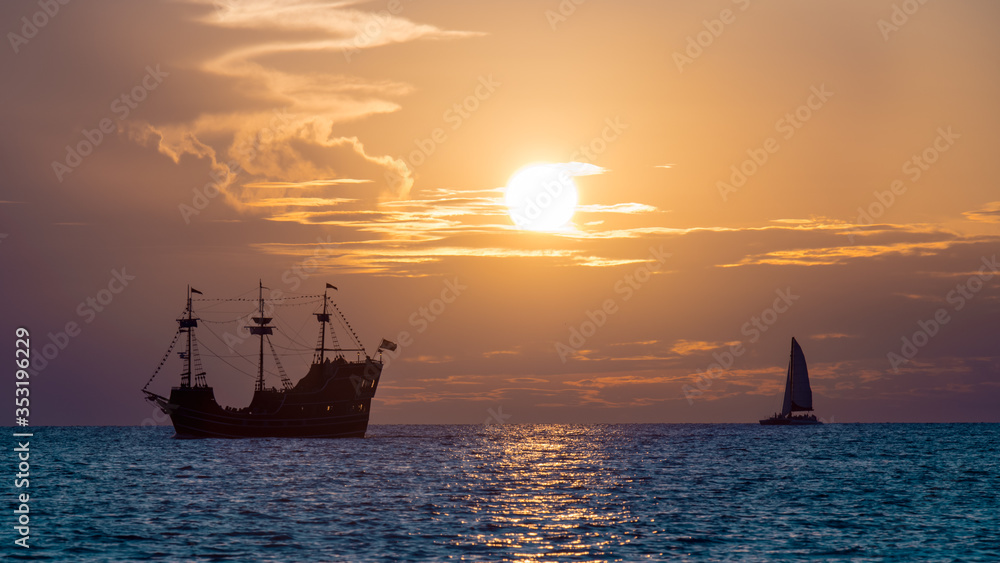 Pirate ship on horizon. Retro or antique sailboat. Ocean sunset. Sunny glare on the water.