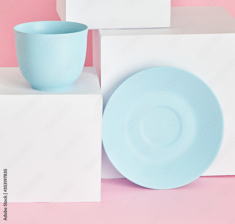 minimalism concept with light pastel colored blue cups and plate with white paper cubs on pink background. minimalism concept with light pastel colored blue cups and plate with white paper cubs on pink background.