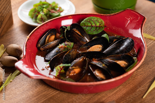 mussels in tomato sauce in a deep plate on a wooden table. close-up