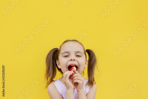 a cheerful girl of 4-5 years old eats fresh strawberries in the fresh air. Summer season. Childhood. Isolated yellow background