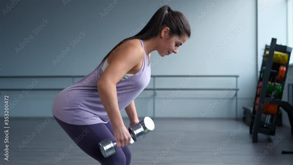 A beautiful athletic young brunette woman in sportswear trains with a dumbbells in the gym. Copy Space. A beautiful athletic young brunette woman in sportswear trains with a dumbbells in the gym. Copy Space.
