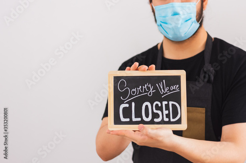 person with facial mask holds a sign saying "sorry we are closed" on a white background