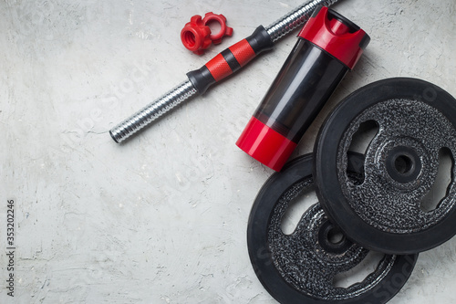 iron Dumbbell and whey protein shaker. Fitness or bodybuilding concept background. Product photograph on grey, concrete floor top view 