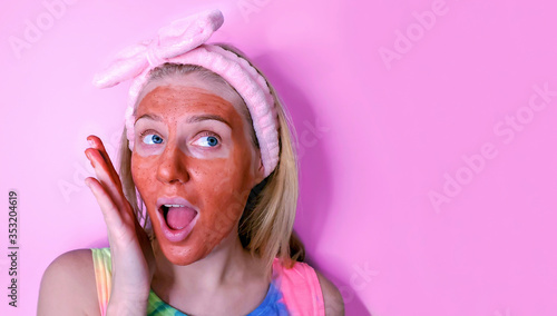 Home skin care. Young woman with clay mask on her face and hair band on head touching her skin gently