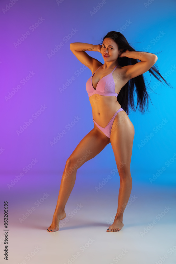 Fashion portrait of young fit and sportive brunette woman with blowing hair in purple swimwear on gradient background. Longhair model. Perfect body ready for summertime. Beauty, resort, sport concept. Fashion portrait of young fit and sportive brunette woman with blowing hair in purple swimwear on gradient background. Longhair model. Perfect body ready for summertime. Beauty, resort, sport concept.