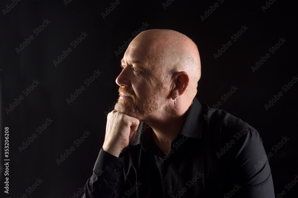 portrait of a man in low key, smiling and looking side with hand on chin portrait of a man in low key, smiling and looking side with hand on chin