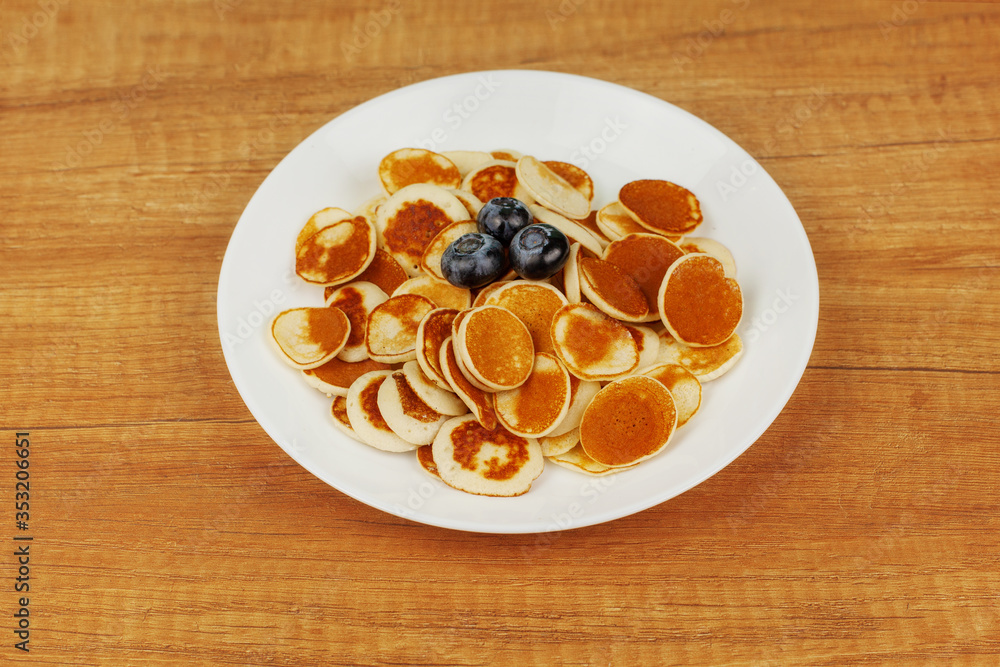 Mini pancakes with blueberries lie in a plate on a wooden table with space for text. Trending food, healthy Breakfast, Breakfast for the whole family Mini pancakes with blueberries lie in a plate on a wooden table with space for text. Trending food, healthy Breakfast, Breakfast for the whole family