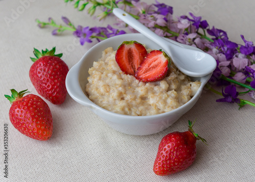 Homemade oatmeal with strawberries in a white plate. Healthy breakfast. Oatmeal with sliced ​​strawberries.