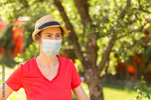Portrait of a beautiful girl in her backyard on a sunny day wearing a surgical mask because of the coronavirus epidemic. Home life during quarantine or self-isolation