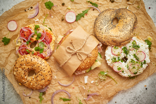 Bagels with ham, cream cheese, hummus, radish wrapped in brown baking paper ready for take away