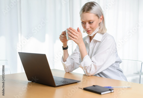  A young girl works with a laptop at home or in the office. antiviral mask.