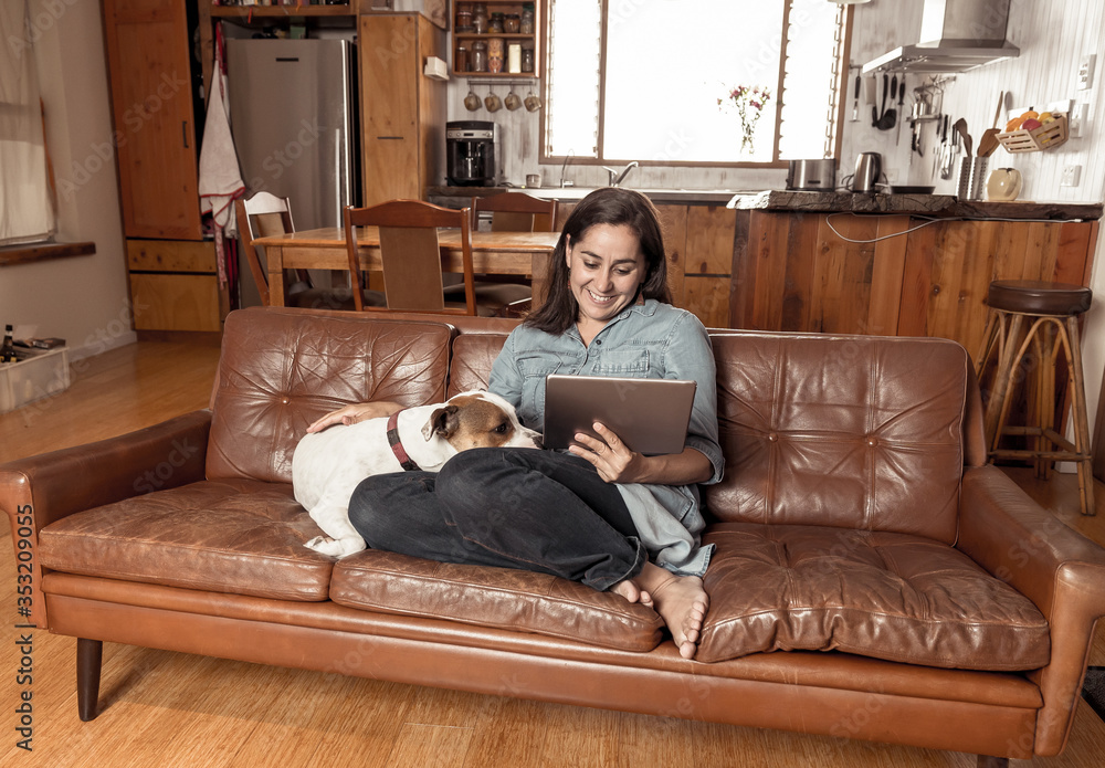 Obraz premium Woman Working from home using laptop with pet dog sitting next to her